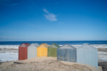 The cold northern sea with a sandy shore on a sunny day was partially freed from winter snow and ice, on the shore there are colorful technical wooden houses