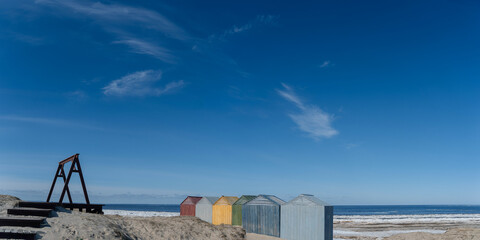 The cold northern sea with a sandy shore on a sunny day was partially freed from winter snow and ice, on the shore there are colorful technical wooden houses