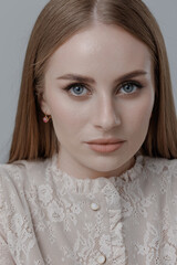Elegant portrait of a woman in a lace blouse with neutral makeup against a simple gray background