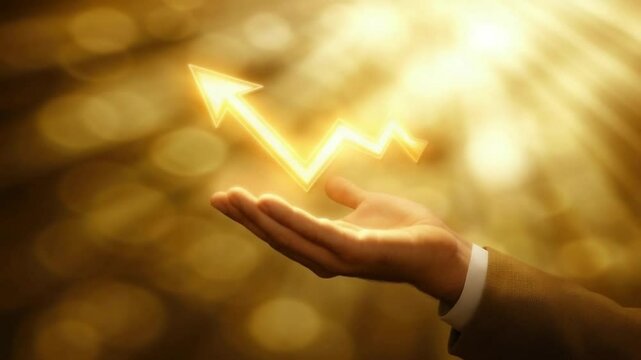 A hand extends forward, showcasing a glowing upward arrow. The shimmering golden background highlights themes of financial growth, success, and positive trends in business or investments