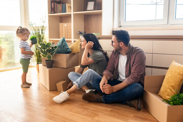 Happy family moving into new home. Young man and woman, parents of small baby girl, having fun with...
