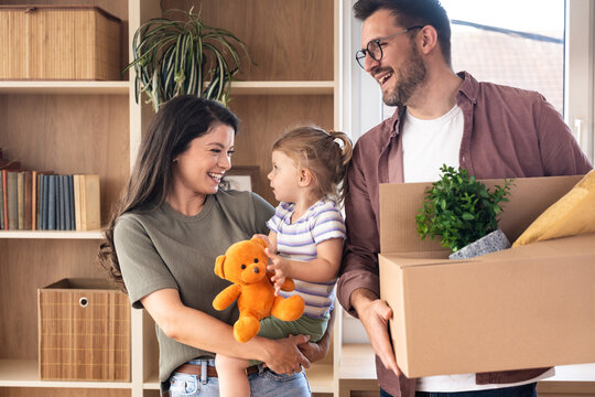 Happy family moving into new home. Young man and woman, parents of small baby girl, having fun with their child, while unpacking cardboard boxes starting their new independent life at new apartment.