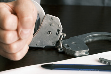 A person is holding a pair of shiny handcuffs over a piece of paper