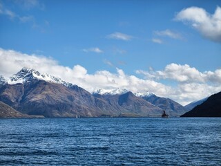 A scenic view of Lake Wakatipu in New Zealand, featuring boats on the water surrounded by snow-capped mountains under a clear blue sky.