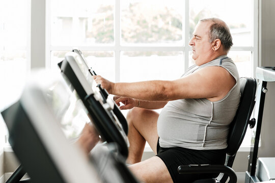 Overweight senior man working out on a stationary bike at the gym, promoting wellness and a healthy lifestyle. Fitness, determination, and aging well through regular exercise and self-care.