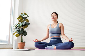 Woman in yoga pose meditating peacefully indoors on a pink mat, wearing fitness clothing, representing mindfulness, mental clarity, wellness routine, and a calm, healthy lifestyle in natural light.
