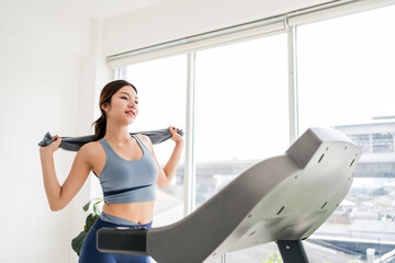 Confident young woman exercising indoors on a treadmill, smiling post-workout while holding a towel. Captures healthy lifestyle, fitness motivation, and wellness in a bright home gym setting.