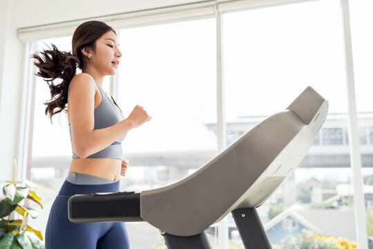 Focused young woman running on a treadmill in a bright modern room, capturing dedication to fitness, cardio training, and healthy lifestyle for wellness, weight loss, and daily exercise routine.