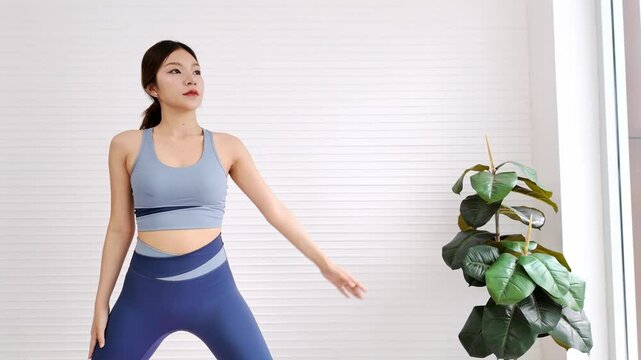 Woman performs side-stretch yoga on a pink mat by tall windows in a bright indoor studio. Her pose emphasizes flexibility, strength, and calmness, promoting fitness and mindful living.