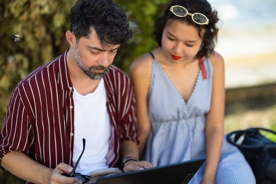 Couple enjoying a relaxed outdoor reading session together, sitting comfortably with a book in a peaceful park setting on a sunny day