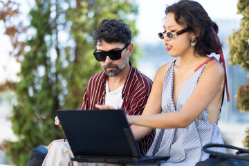 Two stylish young adults collaborating on a laptop outdoors in a casual setting