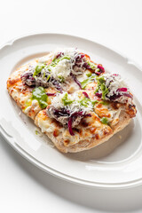 A gourmet open-faced sandwich with melted cheese, shredded meat, red onions, green sauce, and grated cheese on a white plate. Vibrant colors and textures enhance the dish’s visual appeal