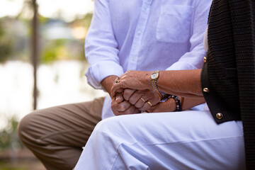 Senior couple sitting on park bench holding hands.