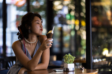 Woman enjoying an ice cream cone in a cafe while relaxing in casual summer attire with a serene expression