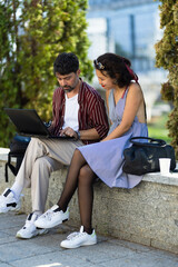 Casual outdoor meeting with man and woman using laptop on sunny day with greenery