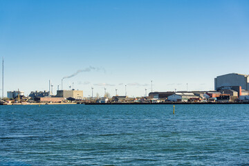 Industrail waterfront with factory building, wind turbine and smoke emitted from chimney on sunny day