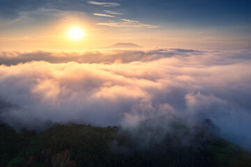 Fototapeta premium Golden sunrise over sea of fog and mountain peak at tropical forest