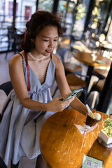 Woman enjoying ice cream in a modern cafe while browsing her phone, capturing a moment of relaxation and leisure time in a stylish setting