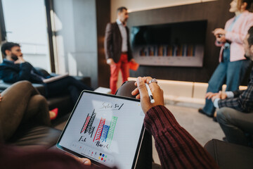 Group of business professionals engaging in a meeting, with focus on a digital tablet displaying sales growth diagrams, within a modern office setting.