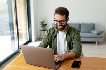 Fototapeta premium Smiling man working from home using laptop