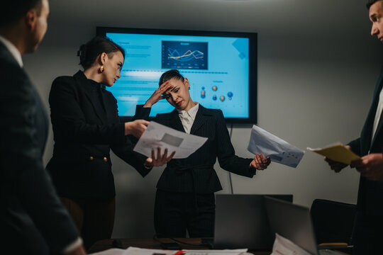 Group of professionals analyzing complicated data in a modern office setting to strategize performance improvements and collaboration. The team appears tense and overburdened, reflecting work