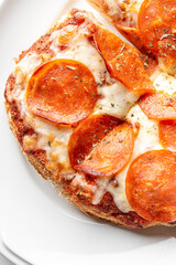 Close-up of a freshly baked pepperoni pizza slice with melted mozzarella cheese, sprinkled with herbs, served on a white plate. The crispy crust and rich tomato sauce enhance its appetizing appearance