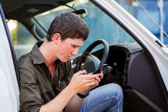 teenaged Australian young man sitting in his ute holding mobile phone device frowning