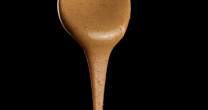 Almond nut butter dripping from a spoon on a black background.
