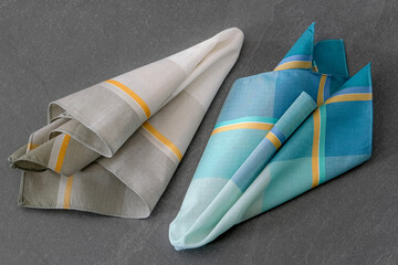 Set of folded handkerchiefs for men with a striped design is placed on a dark stone surface.