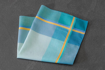 Elegant folded handkerchief with striped design, displayed on a dark stone surface. Suitable for concepts related to men’s fashion accessories, style, or fabric textures.
