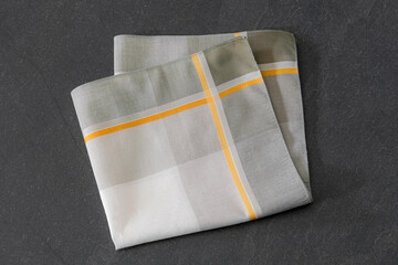 Elegant folded handkerchief with striped design, displayed on a dark stone surface. Suitable for concepts related to men’s fashion accessories, style, or fabric textures.
