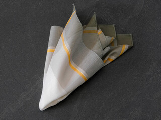 Elegant folded handkerchief with striped design, displayed on a dark stone surface. Suitable for concepts related to men’s fashion accessories, style, or fabric textures.