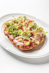 A golden, crispy Roman-style pinsa with a light, airy crust, topped with fresh greens, sliced tomatoes, melted cheese, and creamy dressing, served on a white plate for a delicious meal.