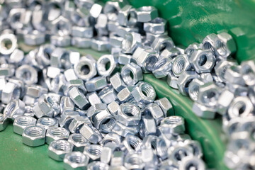 Hex Nuts on Vibratory Feeder Bowl in Factory. Macro view of shiny hexagonal metal nuts being aligned and sorted on a green vibratory feeder in an automated industrial environment. Selected focus