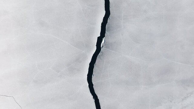 Drone view of a crack with water splitting an icy frozen surface into two parts