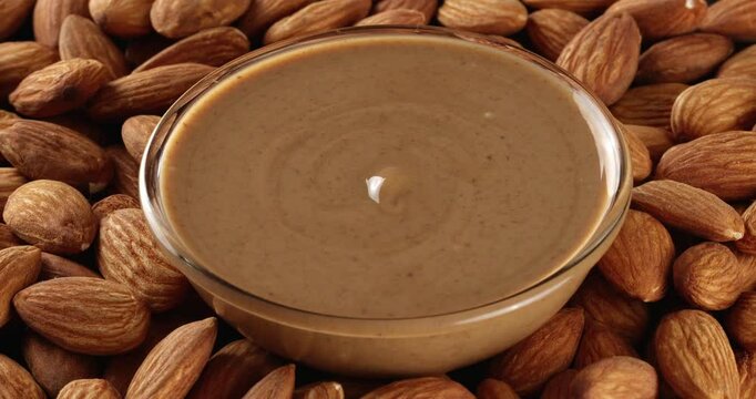 Almond nut butter in a glass bowl on a background of almonds. Close-up footage on the rotating table.