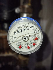 Blue water meter connected to pipes on blurred background shows water consumption.
