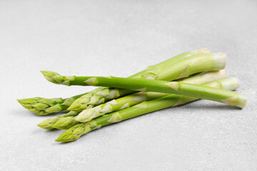 Bunch of raw fresh green asparagus stalks on light gray textured background. Healthy food, fresh produce, cooking ingredient, vegetarian recipe, or organic farming, agriculture.