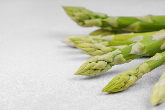Bunch of raw fresh green asparagus stalks macro, close up on light gray textured background with copy space. Healthy food, fresh produce, cooking ingredient, vegetarian recipe, organic agriculture.
