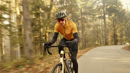 Man rides a bicycle on a scenic forest path, wearing a yellow and black outfit, helmet, and sunglasses. Image is a close-up shot. © stockcopter