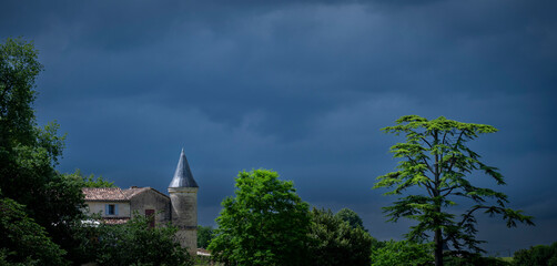 Naklejka premium Chateau Tour Baladoz is nestled among vibrant greenery, showcasing its magnificent architecture against a backdrop of dark clouds in the picturesque Saint-Emilion wine route.