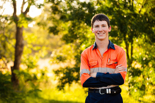 copy space beside young tradesman apprentice in high-vis workwear against leafy green bokeh backdrop