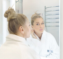 woman looking in the mirror in the bathroom and taking care of her skin.
