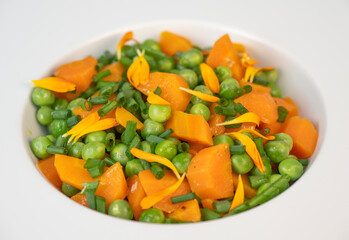 Fresh garden peas and carrots are cooked with salted butter, then garnished with chives and bright marigold flowers for an appealing and colorful side dish.