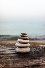 A small pyramid of smooth pebbles rests on a weathered log by the sea