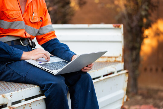 Young trainee tradie apprentice working on laptop in back of ute in high-vis workwear