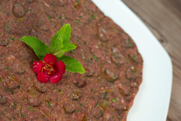 Kebbe naye is showcased on a white plate, featuring finely chopped raw meat mixed with bulgur, onions, mint, and spices, designed for a rich culinary experience.