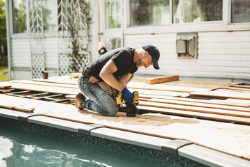 Handyman worker making patio outside close to a pool installing floor.