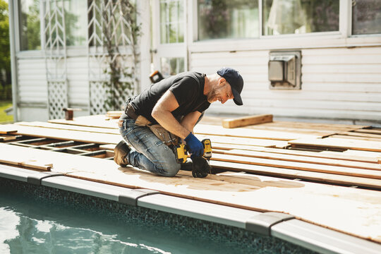 Handyman worker making patio outside close to a pool installing floor.