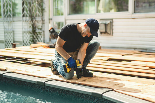 Handyman worker making patio outside close to a pool installing floor.